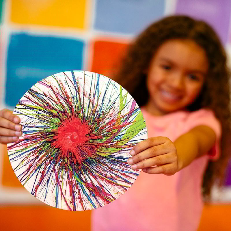 Child holds out a colorful drip art masterpiece